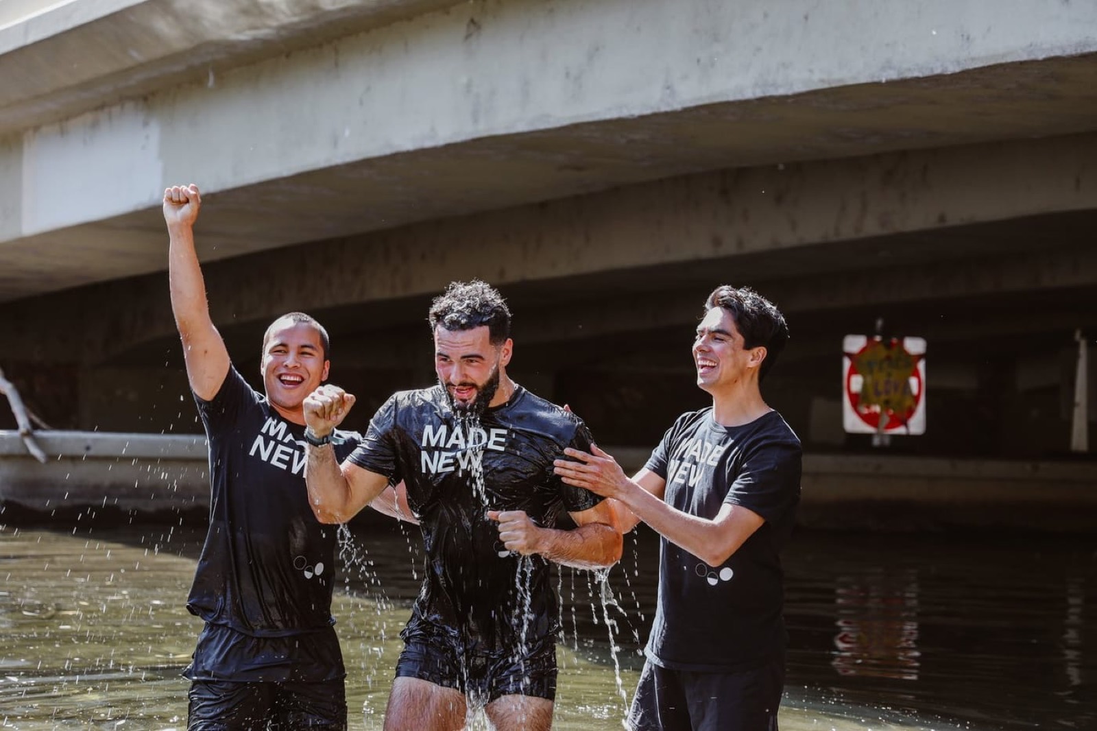 Man cheering in Boulder Creek after his baptism, flanked by two friends