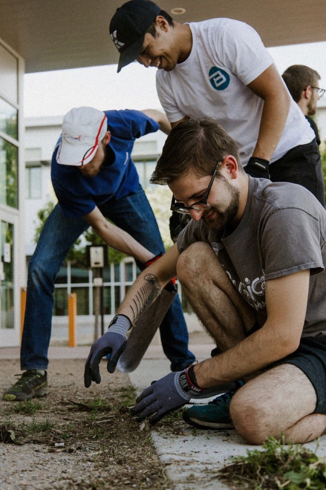 Volunteers kneeling to pull weeds along a sidewalk on a serve day