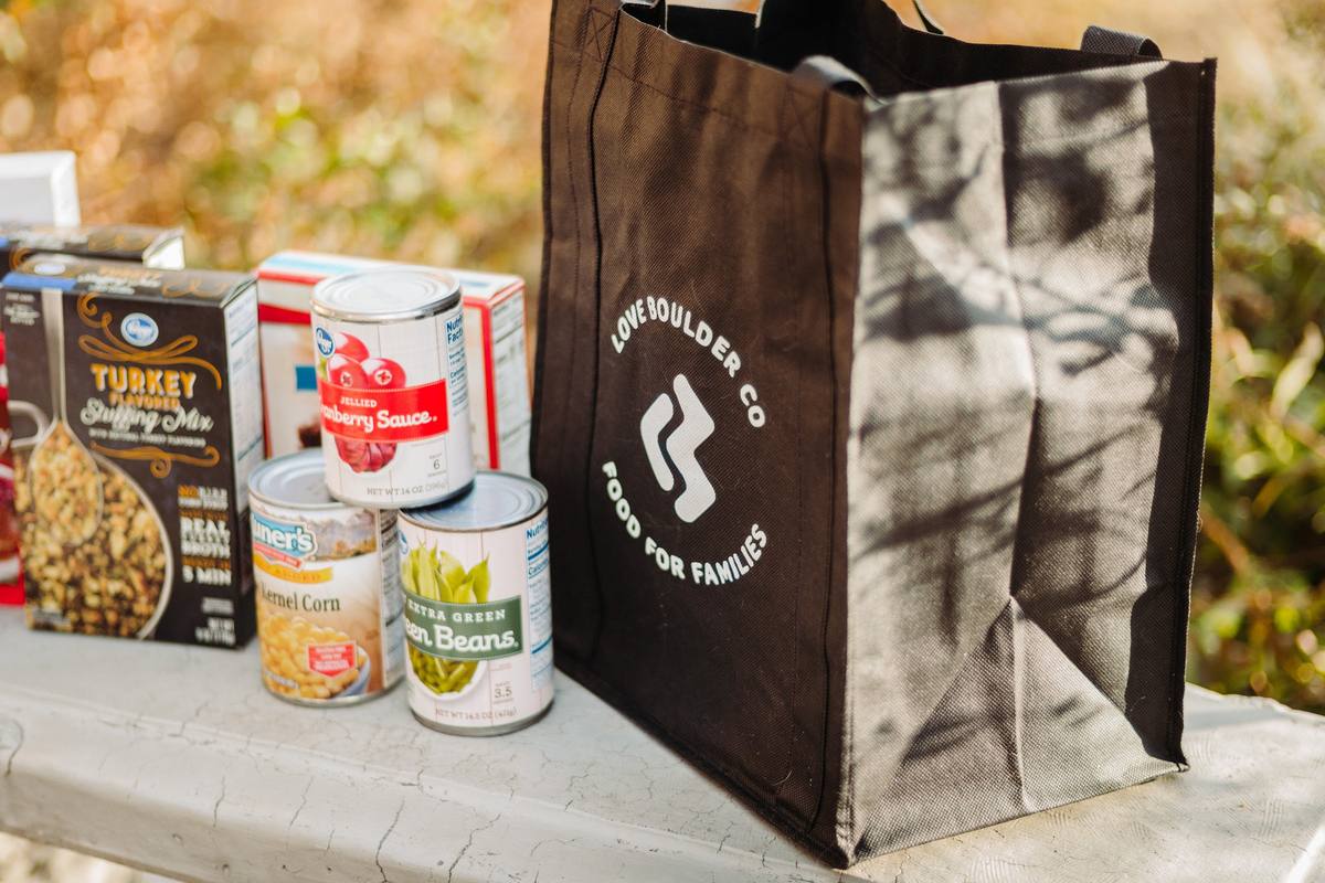 A black Love Boulder Food for Families tote bag beside boxed stuffing mix, cranberry sauce and canned vegetables