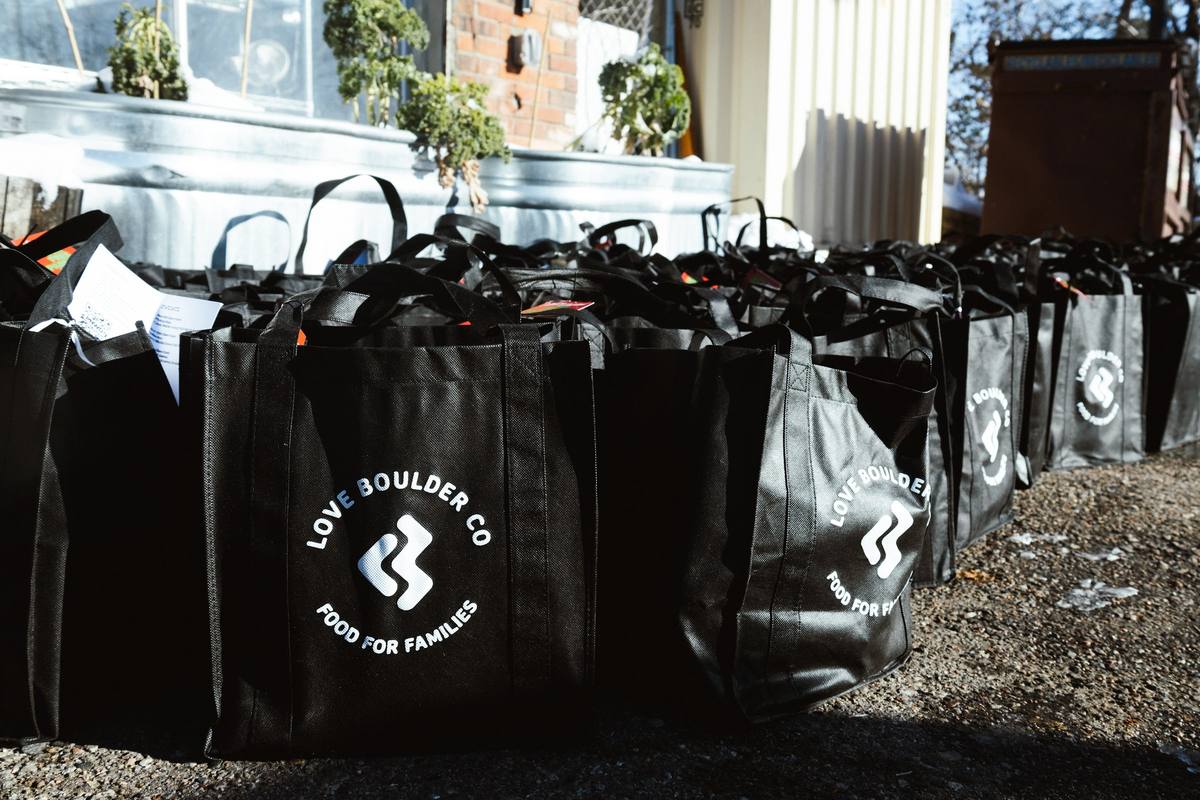 Filled Love Boulder Food for Families bags in a row on gravel, the logo facing out