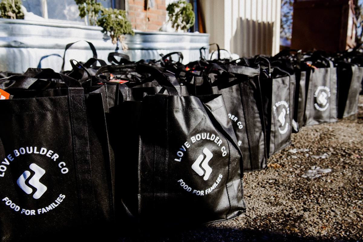 A long row of filled black Love Boulder Food for Families bags lined up outside in the sun