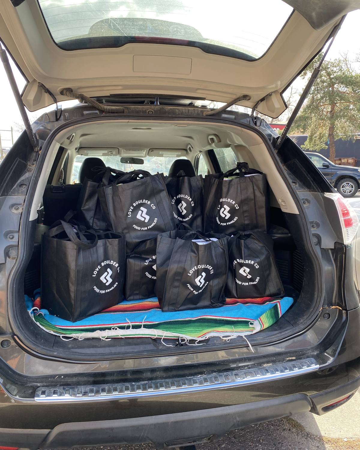The open back of a car packed with black Love Boulder Food for Families bags, ready to deliver