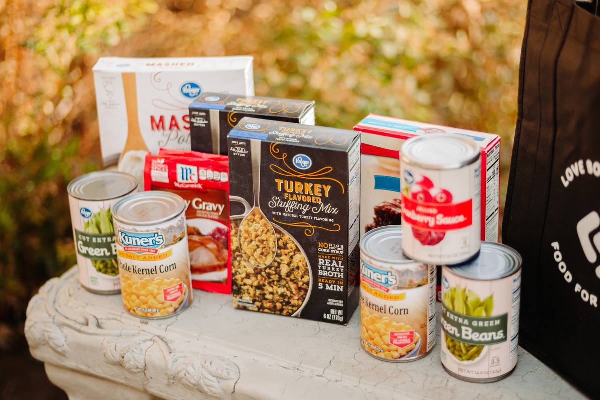 Thanksgiving groceries lined up on a stone bench: stuffing mix, gravy, mashed potatoes, corn and green beans