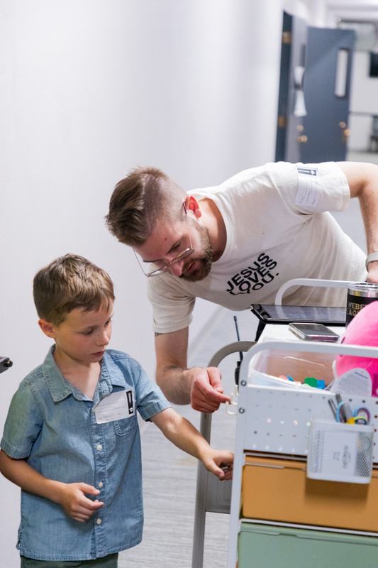 A PNWD Kids leader leaning down to help a boy wearing his name tag at the check-in cart