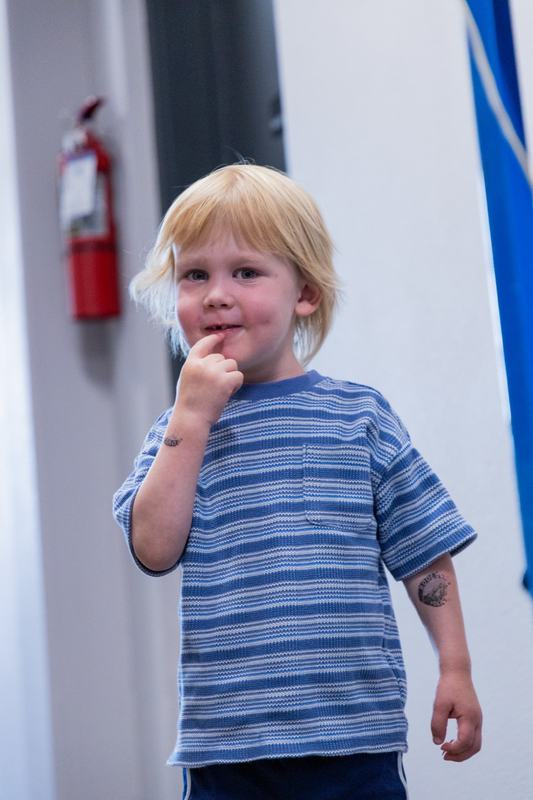 A blond toddler in a blue striped shirt standing in the hallway with a finger to his mouth