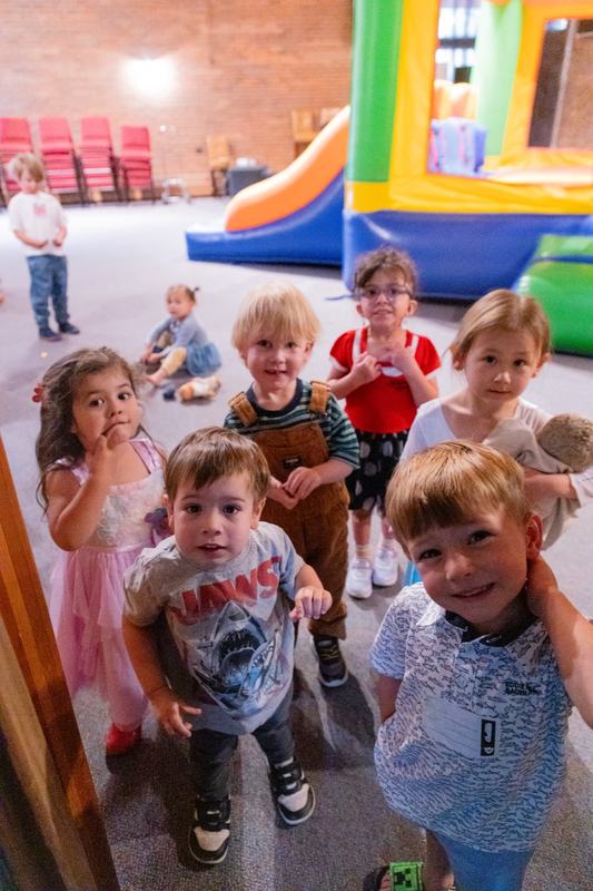 A group of toddlers crowding toward the camera, with a bounce house and slide behind them