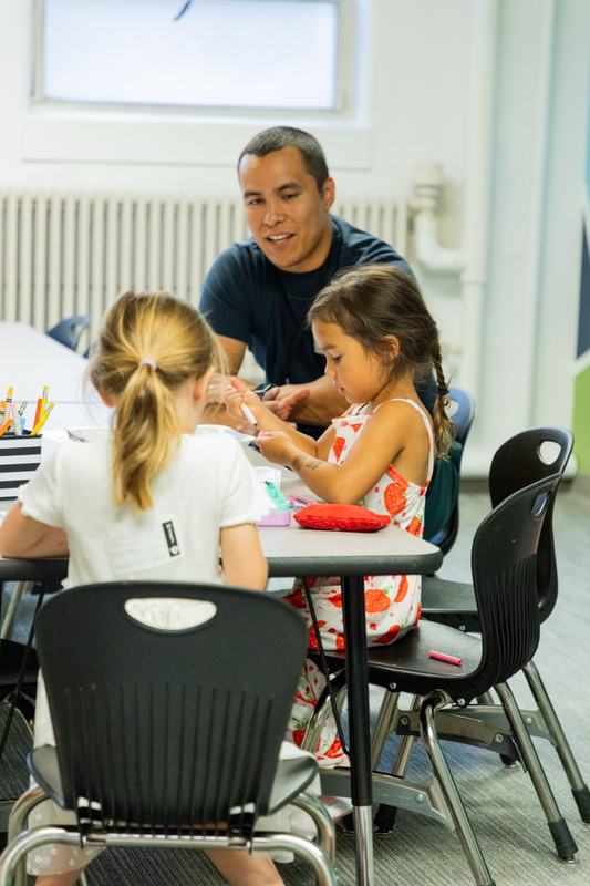 A leader drawing with two girls at a classroom table