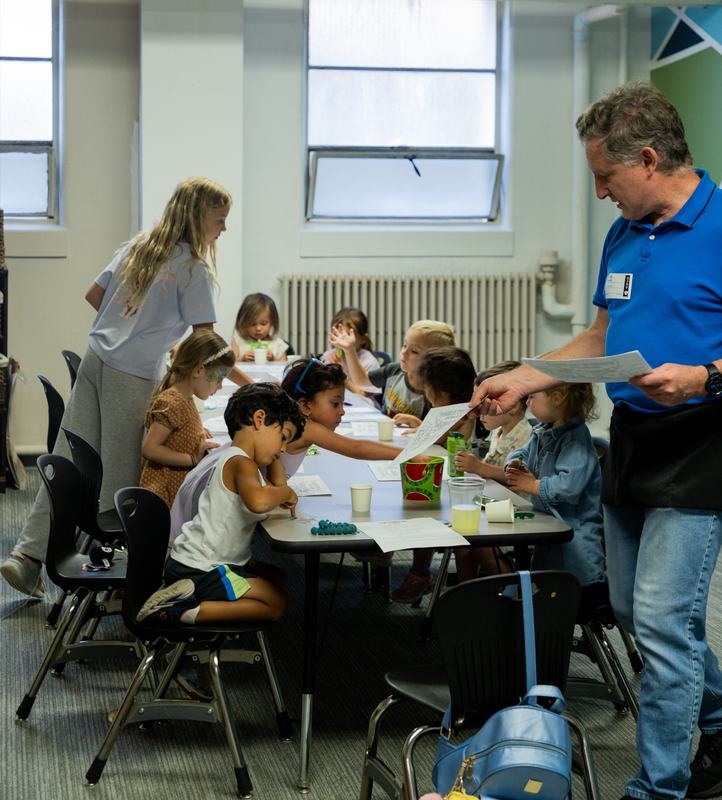 Kids working on papers around a long classroom table while two leaders help