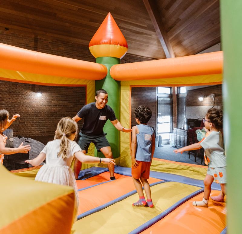 A leader playing with a group of kids inside an orange and green bounce castle