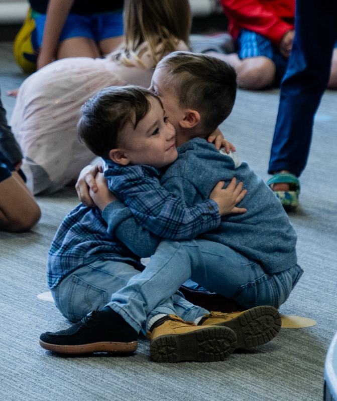 Two little boys hugging while sitting on the classroom floor