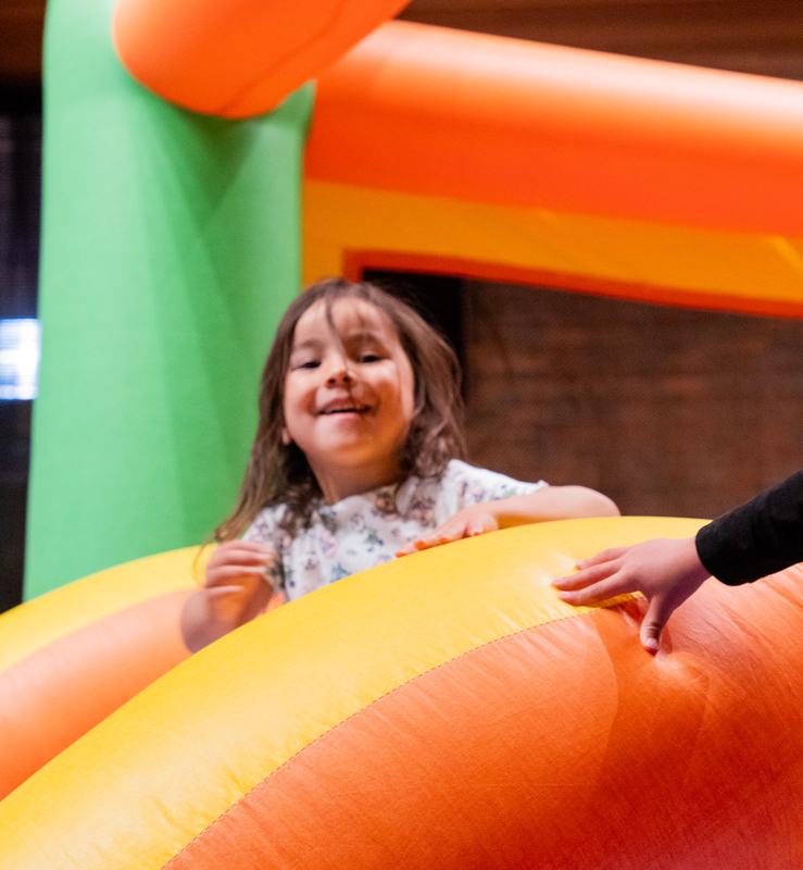 A smiling girl climbing over the edge of an orange bounce house