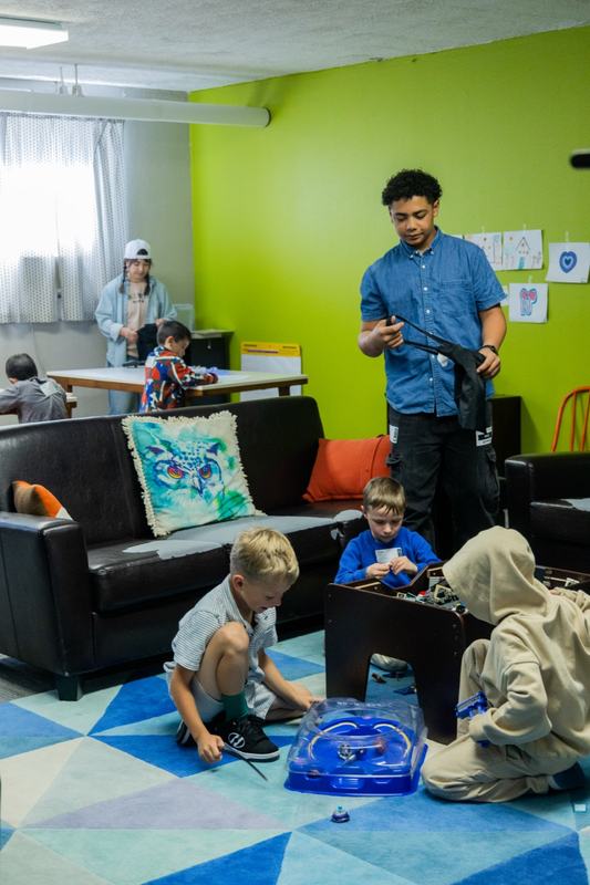 Boys playing a tabletop game on a bright rug while a leader looks on