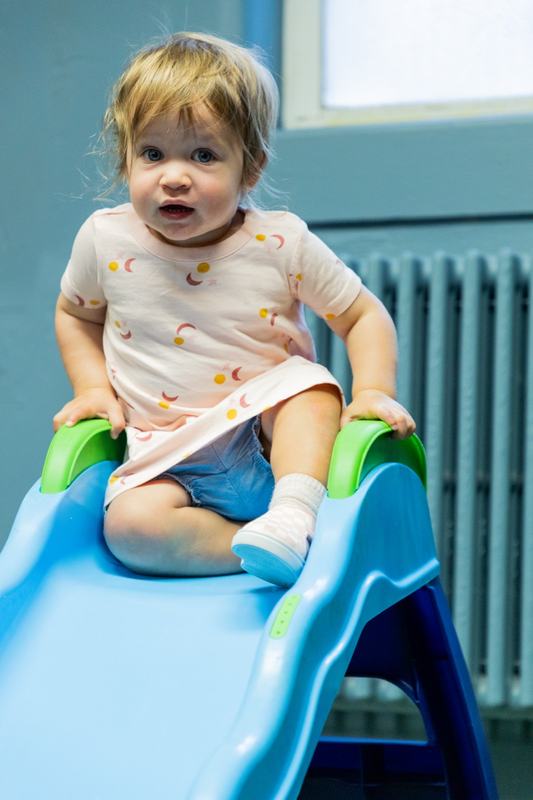 A toddler in a patterned shirt sitting at the top of a small blue slide