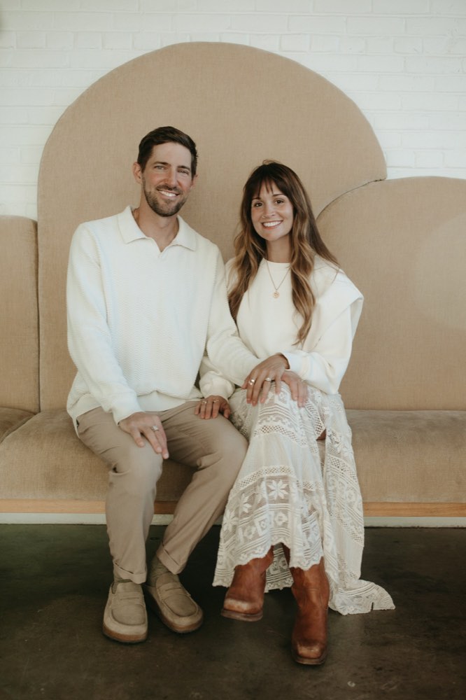 Pastors Parker and Jess Manuel seated together in front of a warm arched backdrop