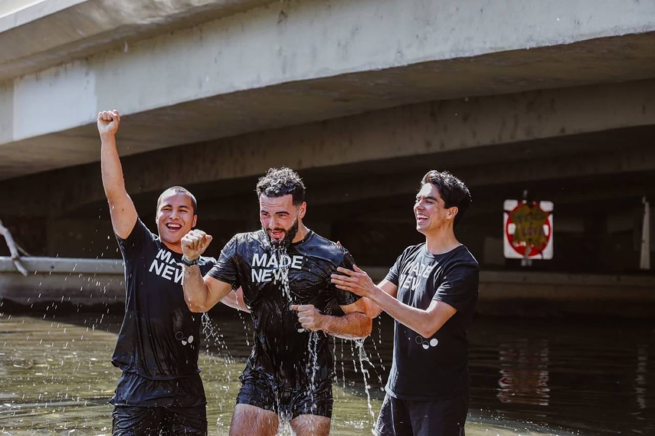 Man cheering in Boulder Creek after his baptism, flanked by two friends