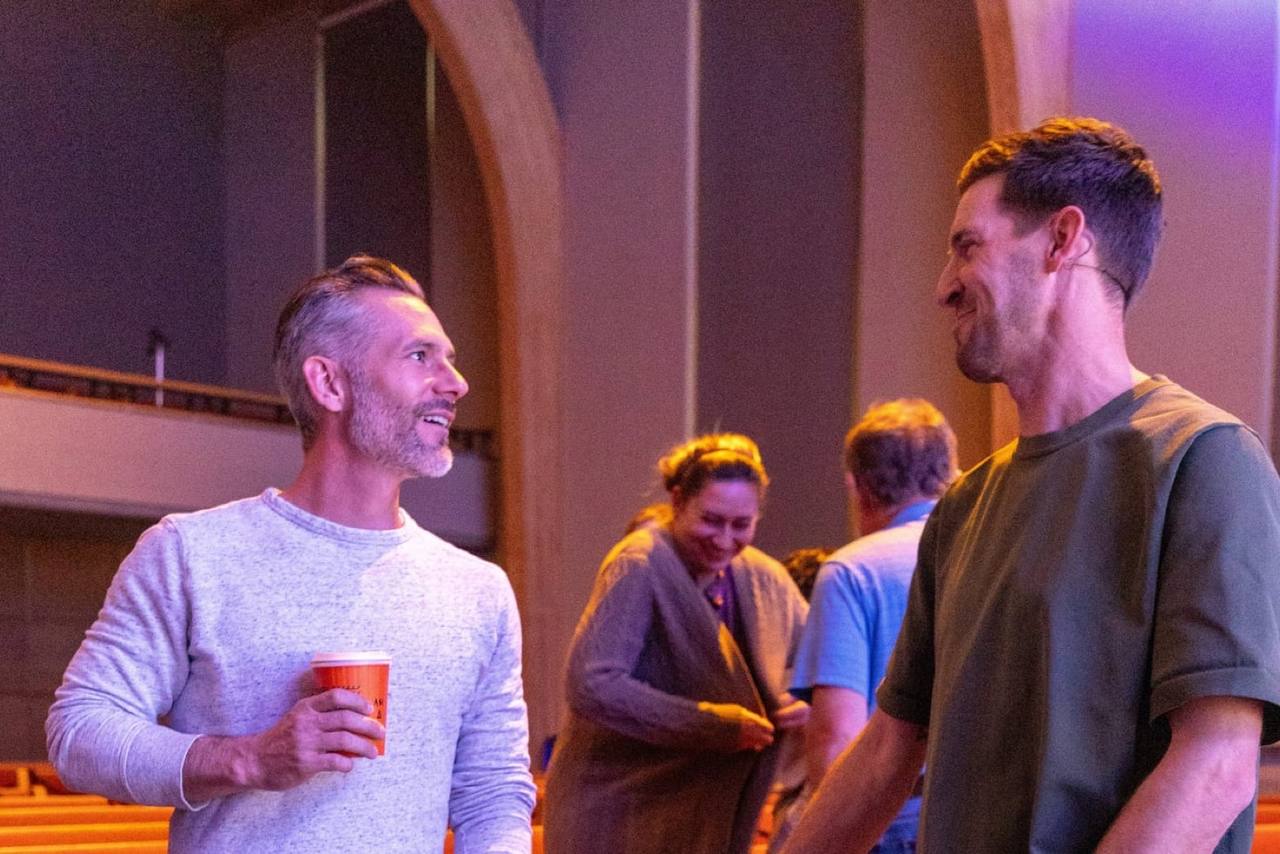 Two men talking and laughing in the auditorium, coffee in hand