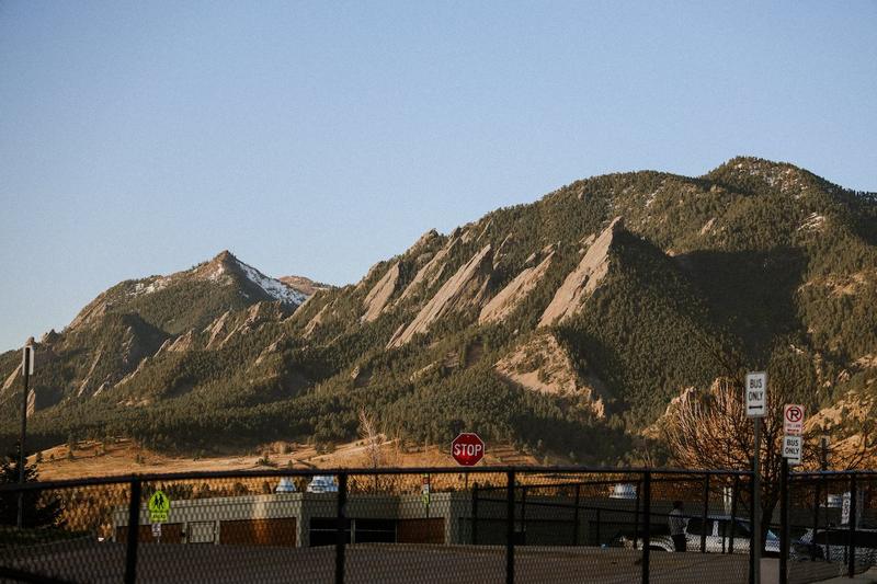 The Flatirons in warm light behind a fenced lot, a stop sign and a bus only sign in the foreground