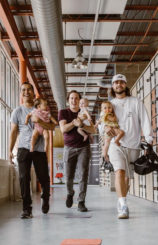 Three smiling men walking down a bright hallway, each carrying a baby