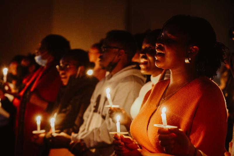 People singing in a darkened room, each holding a lit candle