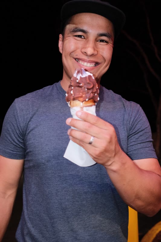 Julian Calderon in a black cap and gray T-shirt, smiling with a chocolate-dipped ice cream cone at night