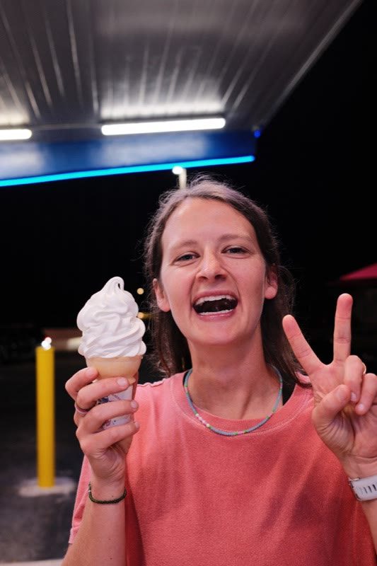 Sara Regan in a coral tank top, laughing and making a peace sign with a vanilla ice cream cone