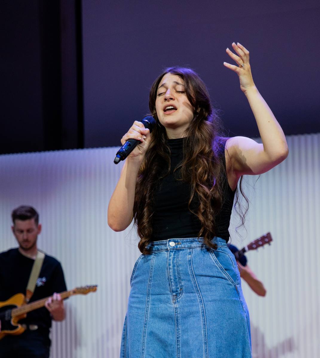 A singer with one hand raised sings with her eyes closed
